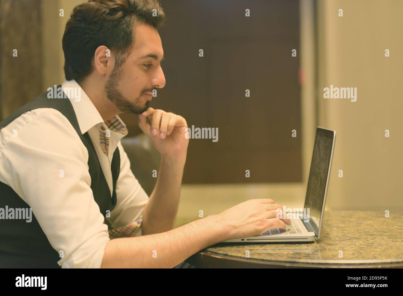Profil anzeigen von jungen schönen Indischen Mann denken, während mit Laptop in der Lobby des Hotel Stockfoto
