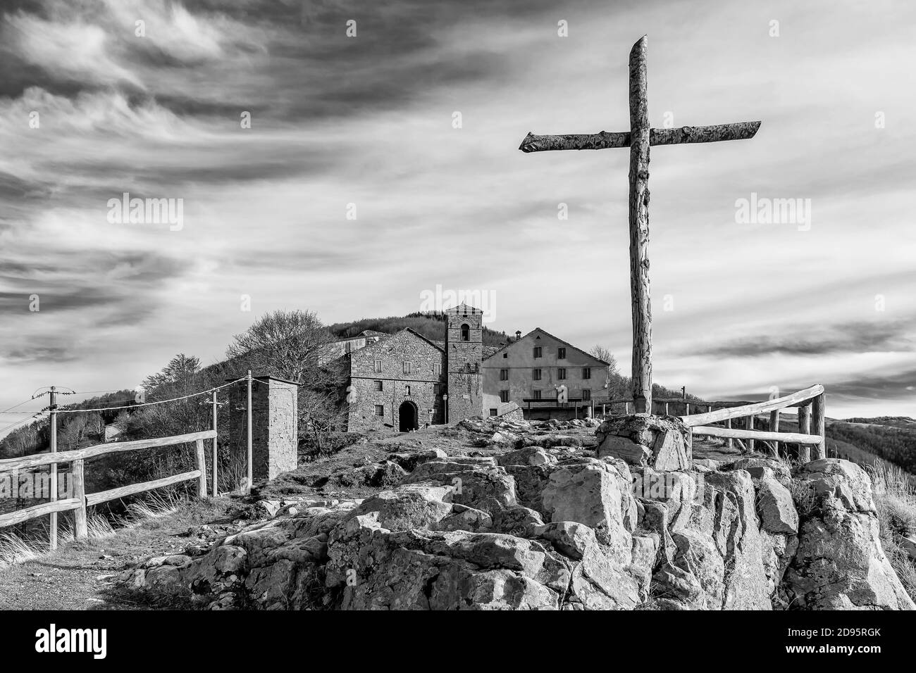 Blick in Schwarz und Weiß auf das Kreuz von San Pellegrino in Alpe mit dem Dorf im Hintergrund, an der Grenze zwischen Toskana und Emilia, Italien Stockfoto