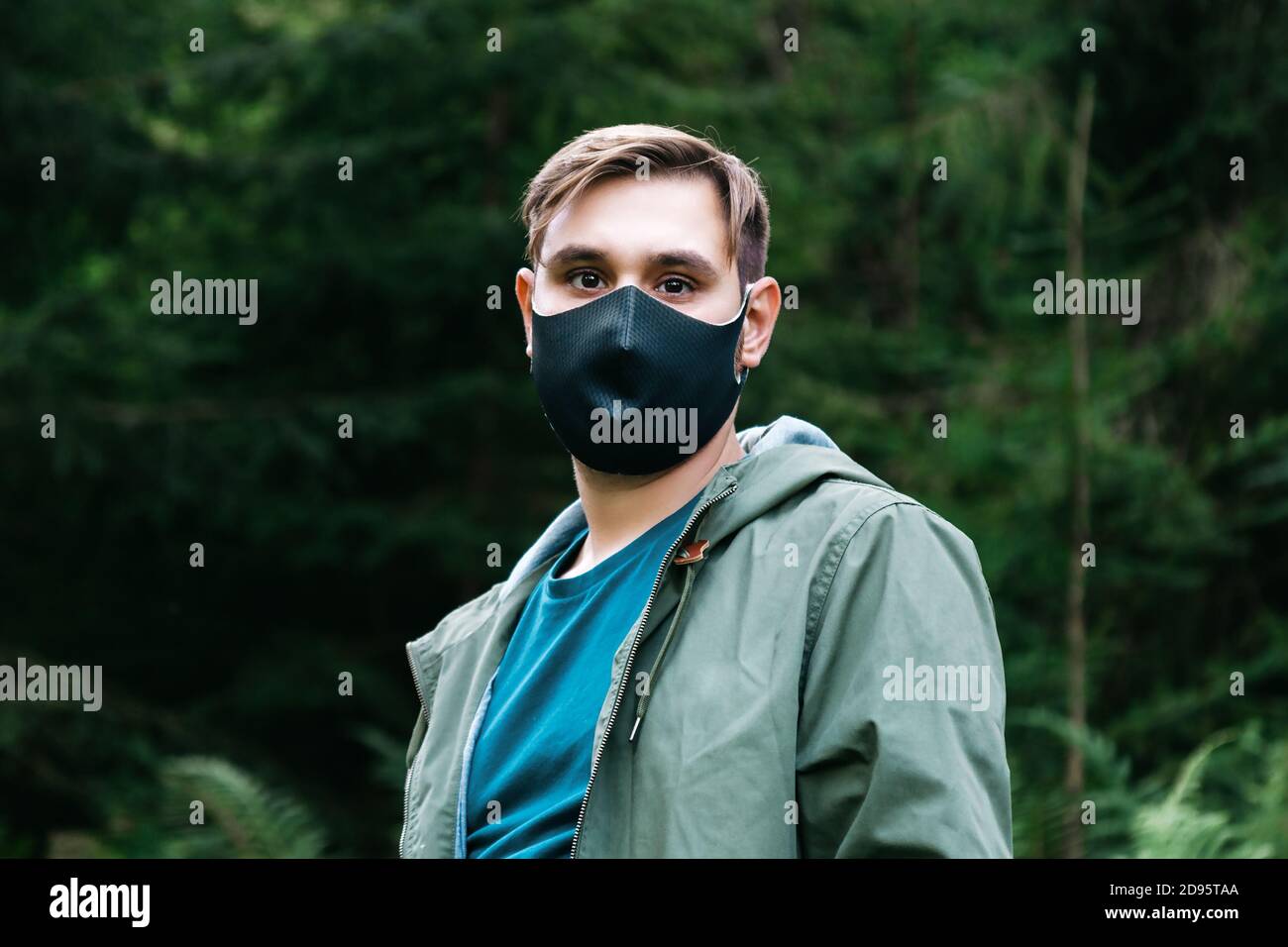 Kaukasischer Mann in schwarzer Schutzmaske außen. Guy Porträt in medizinische Maske auf Waldlandschaft allein halten soziale Distanzierung. Schutz vor Stockfoto