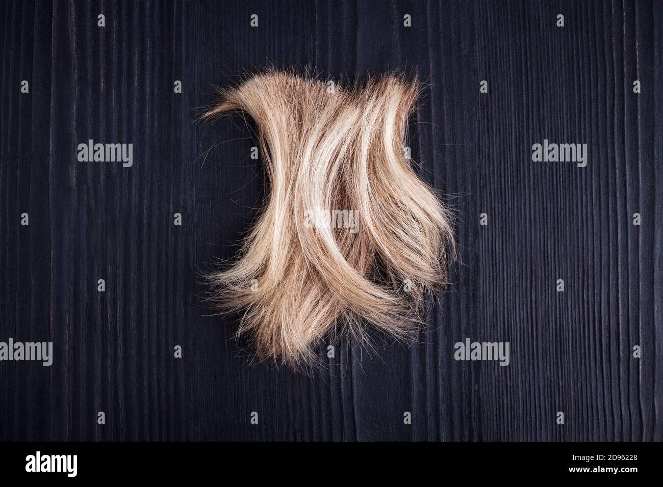 Blonde gewellte Haarsperre schwarzer Holzhintergrund Nahaufnahme, abgeschnitten natürliche blonde Haare Locke auf dunklem Holz, Haarschnitt, Frisur, menschliche Haare schneiden Haare schnippen Stockfoto