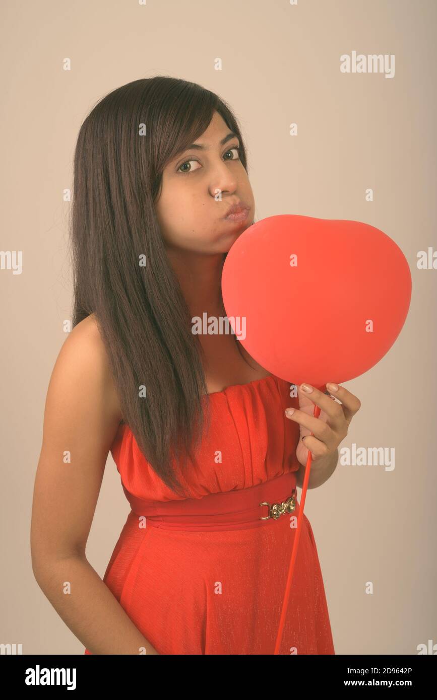 Studio shot der jungen Persischen Frau küssen, während rote herzförmige Ballons für den Valentinstag bereit, gegen grauer Hintergrund Stockfoto