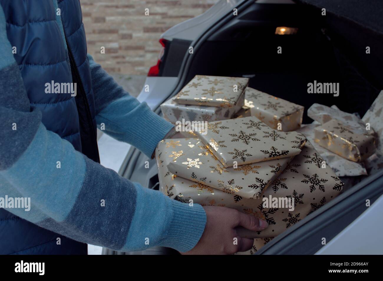 Ein Mann nimmt aus dem Auto Weihnachtsgeschenke, die er gerade gekauft hat, um unter den Weihnachtsbaum zu Hause setzen. Weihnachtsfotografie 2020. Verbraucher. Stockfoto