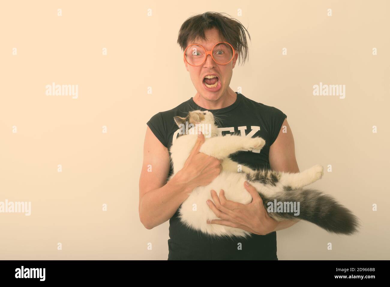 Studio shot Junger nerd Mann aufgeregt suchen, während Sie süße Katze und das Tragen von Brillen vor weißem Hintergrund Stockfoto