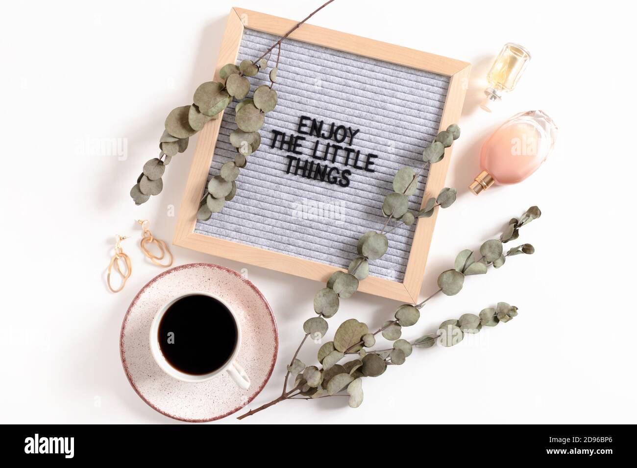Komposition mit Damenaccessoires, Tasse Kaffee, Eukalyptuszweigen und Briefbogen mit Zitat Genießen Sie die kleinen Dinge Stockfoto