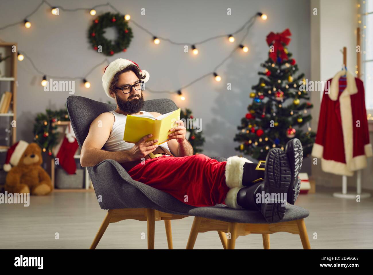 Moderne Santa entspannen in bequemen Sessel zu Hause und Lesen Buch der Geschichten und Märchen Stockfoto