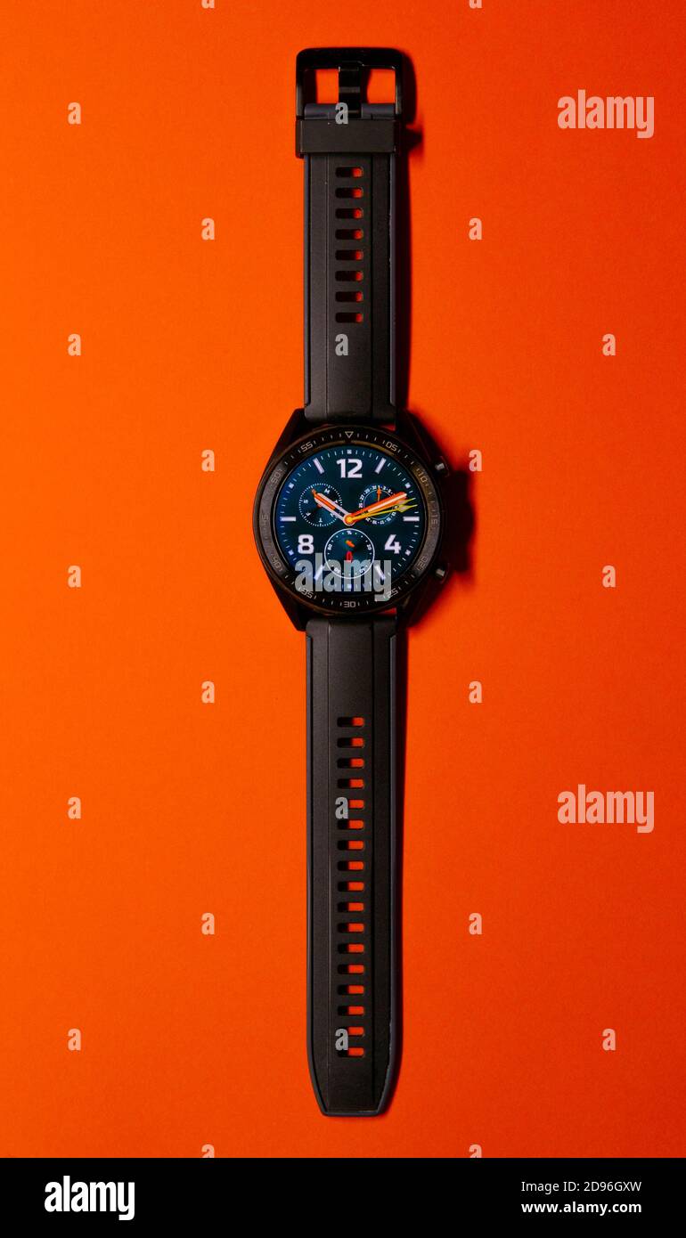 Nahaufnahme einer schwarzen Smartwatch auf orangefarbenem Hintergrund, ähnlich einem Zifferblatt. Technologie und Eleganz Konzept. Vertikale Fotografie. Speicherplatz kopieren Stockfoto