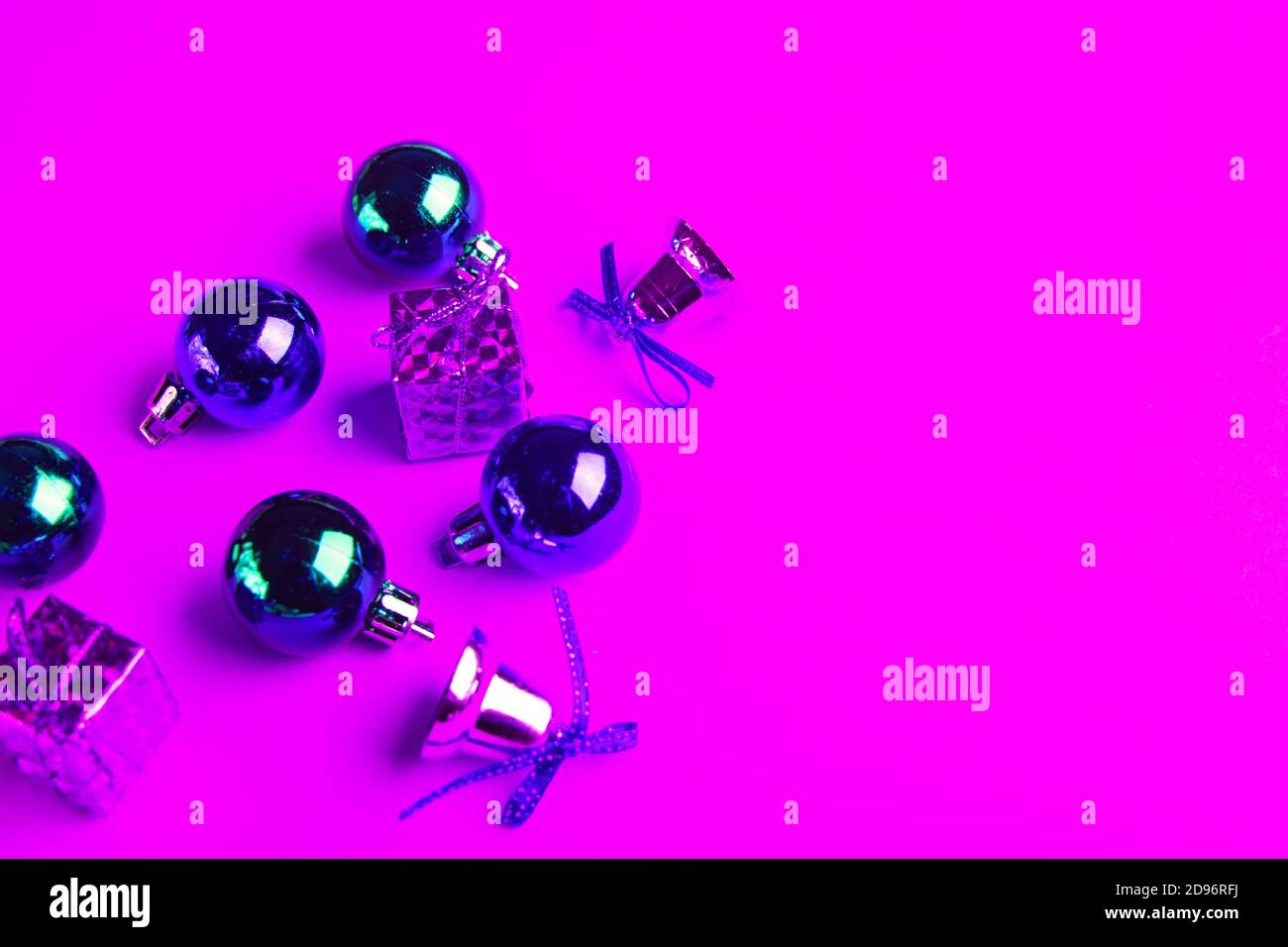 Weihnachtskugeln, Geschenke und funkelnde Glocken in Neonlicht auf rosa Hintergrund. Stockfoto