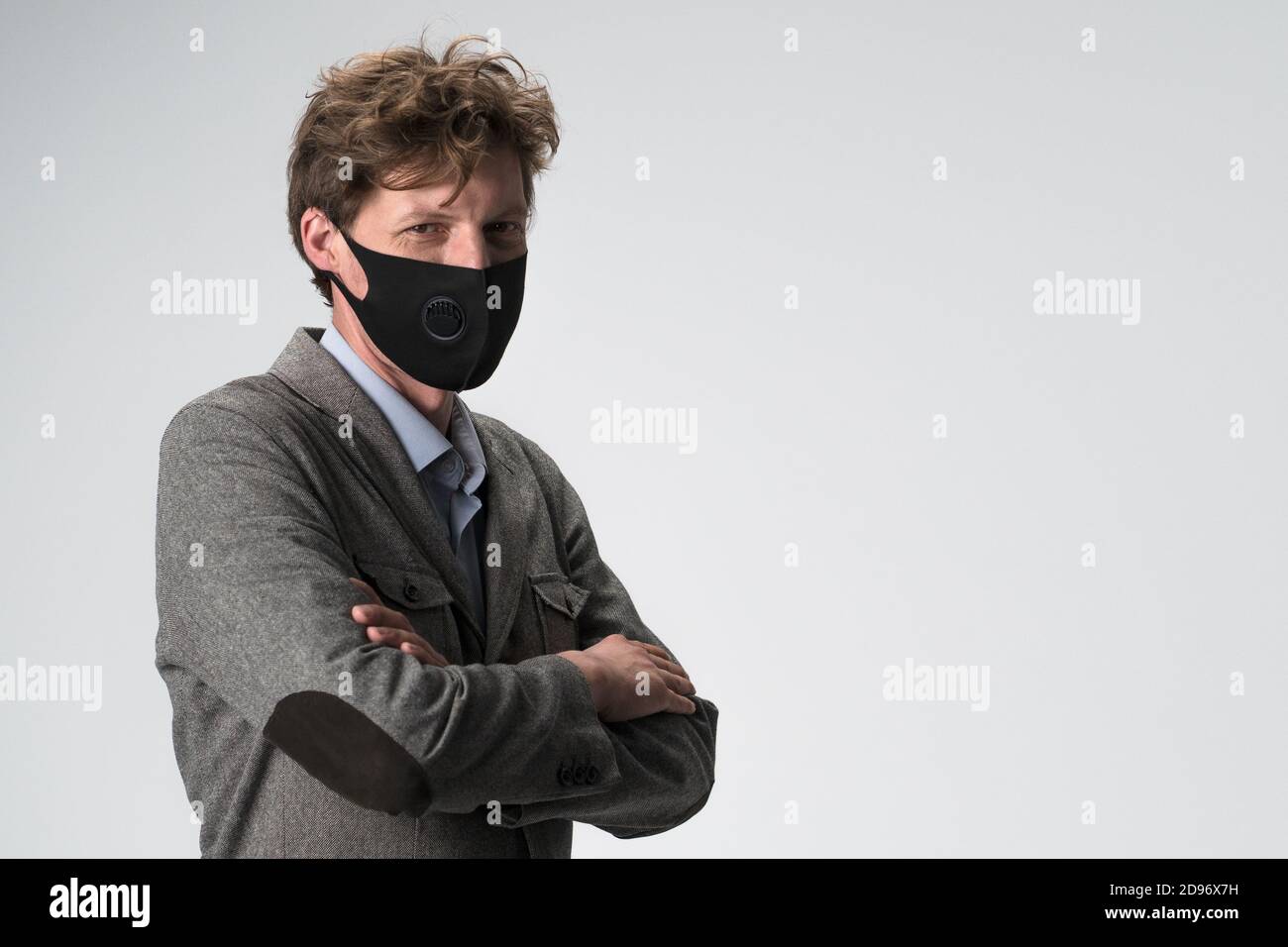 Junger Geschäftsmann in Gesichtsmaske gekreuzte Arme. Selbstbewusster Mann in grauer Jacke posiert auf weißem Hintergrund. Platz auf der rechten Seite kopieren. Stockfoto