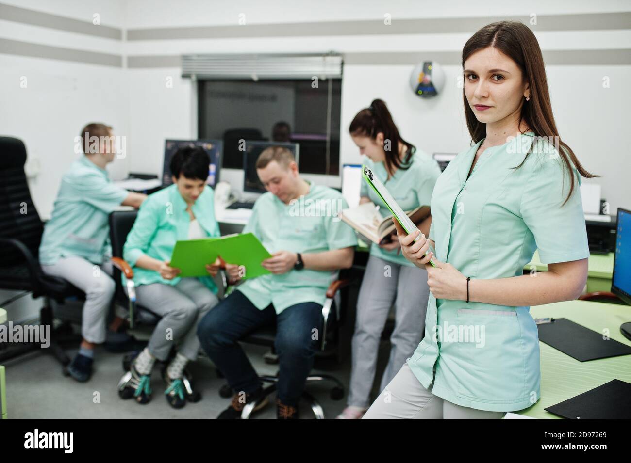 Medizinisches Thema .Porträt der weiblichen Ärztin mit Zwischenablage gegen Gruppe von Ärzten Treffen in der mrt-Büro im diagnostischen Zentrum im Krankenhaus. Stockfoto