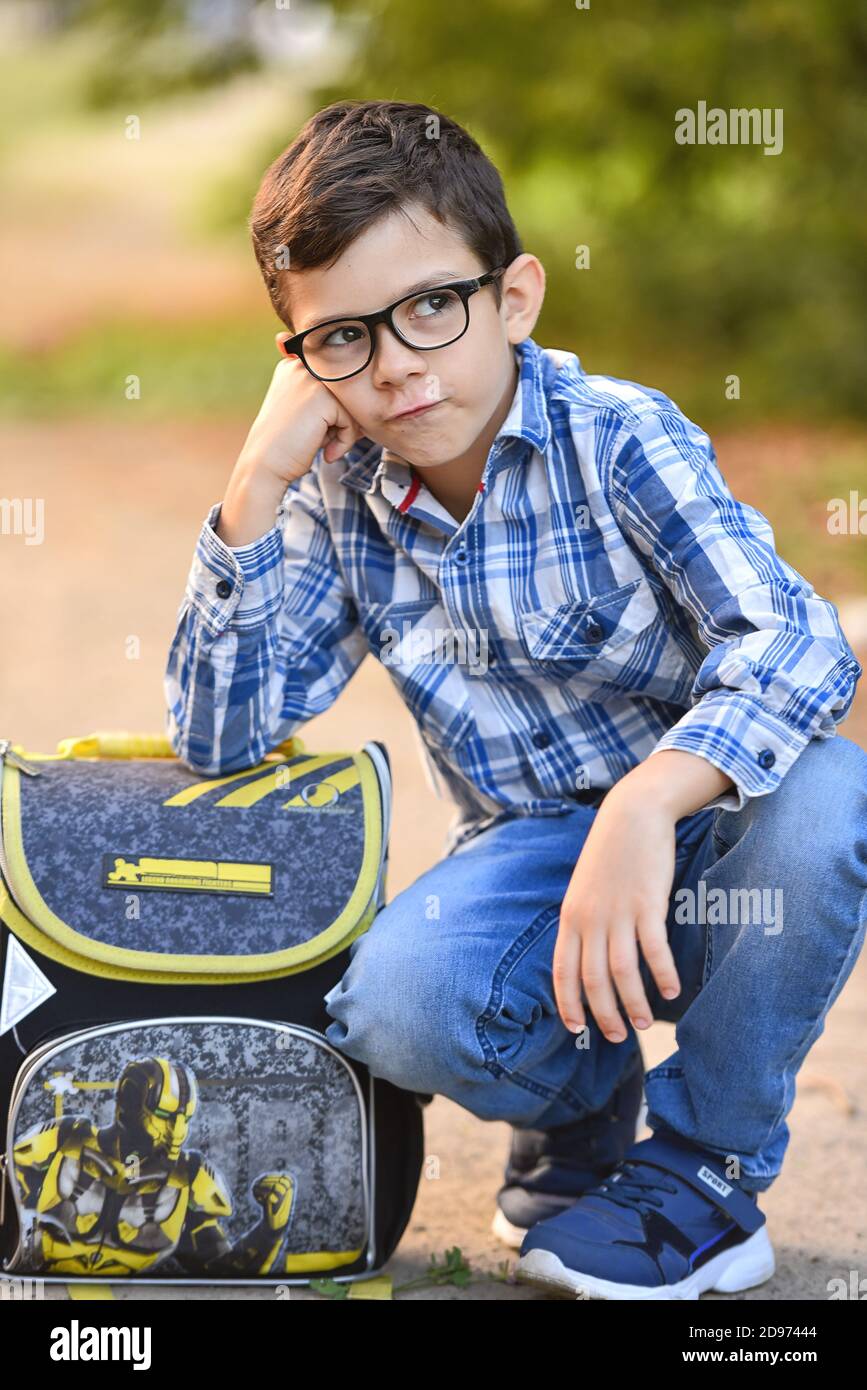 Kaukasische Student Junge mit einer Aktentasche auf dem Boden sitzen, Träume, traurig, niedlich Schuljunge in Jeans und ein Hemd, schöner Hintergrund, EIN schöner Stockfoto