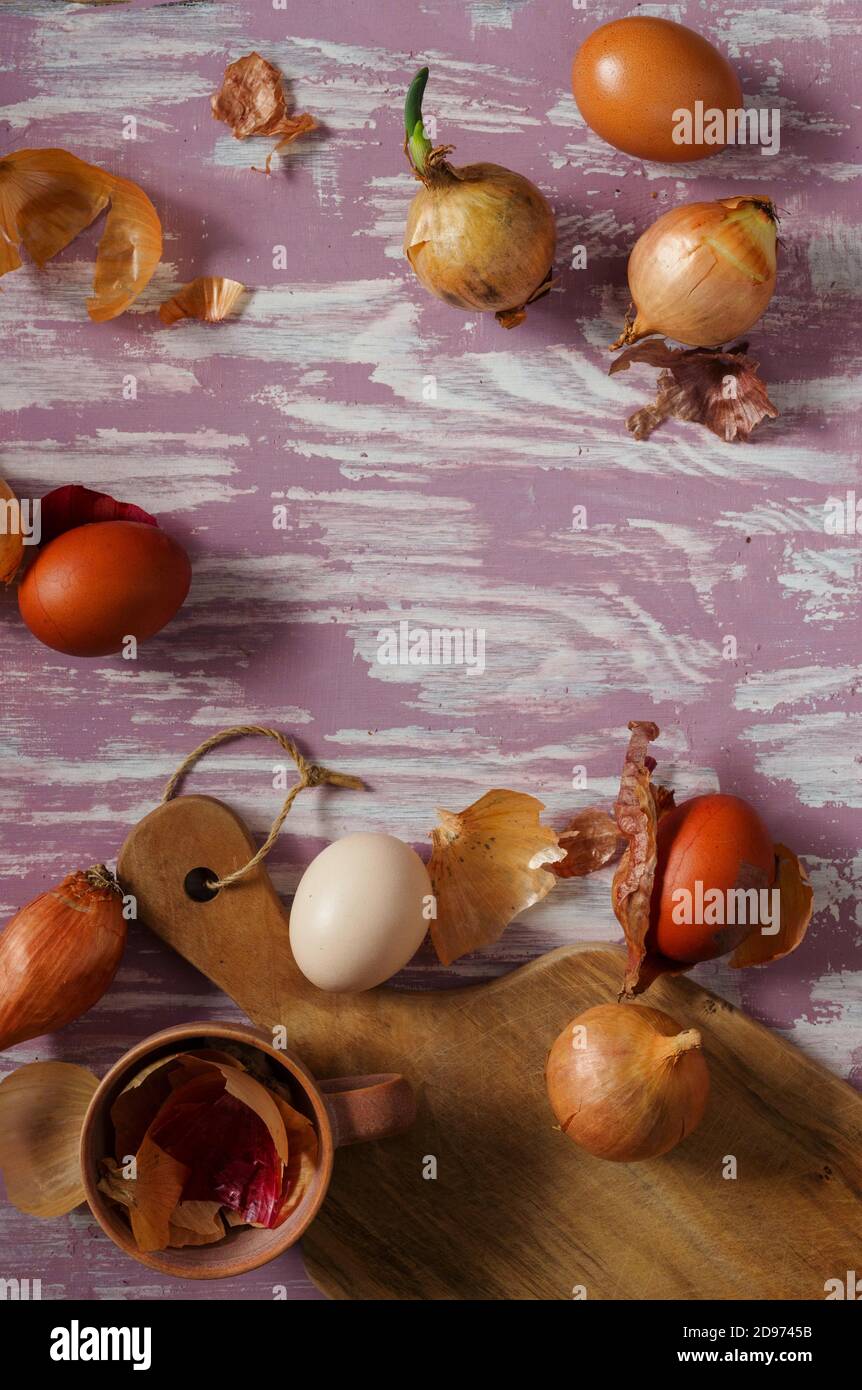 Eier und Zwiebeln auf einem rustikalen Tisch, Blick von oben. Ostereier in traditionellen natürlichen Farbstoff gefärbt - Zwiebelhäute. Polnische Ostertradition. Stockfoto