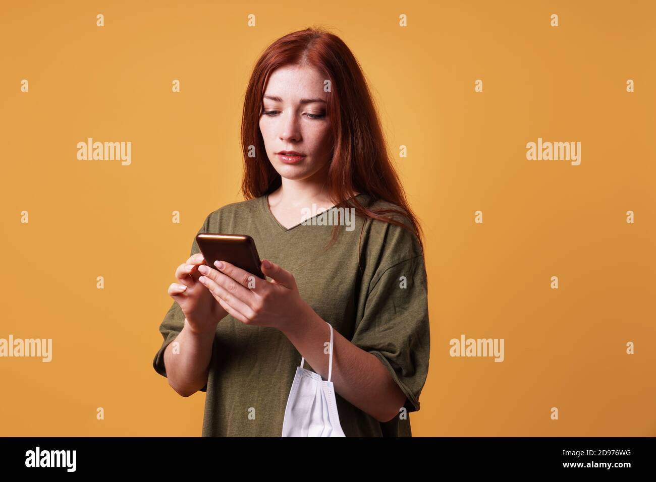 Junge Frau mit ihrem Smartphone oder Handy im Gesicht Maske hängt um ihr Handgelenk Stockfoto