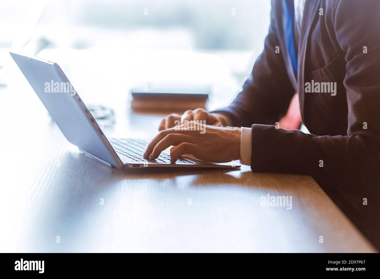 Top-Manager, der am Schreibtisch am Laptop arbeitet. Nahaufnahme der männlichen Arme, die auf der Computertastatur tippen. Seitenansicht Stockfoto