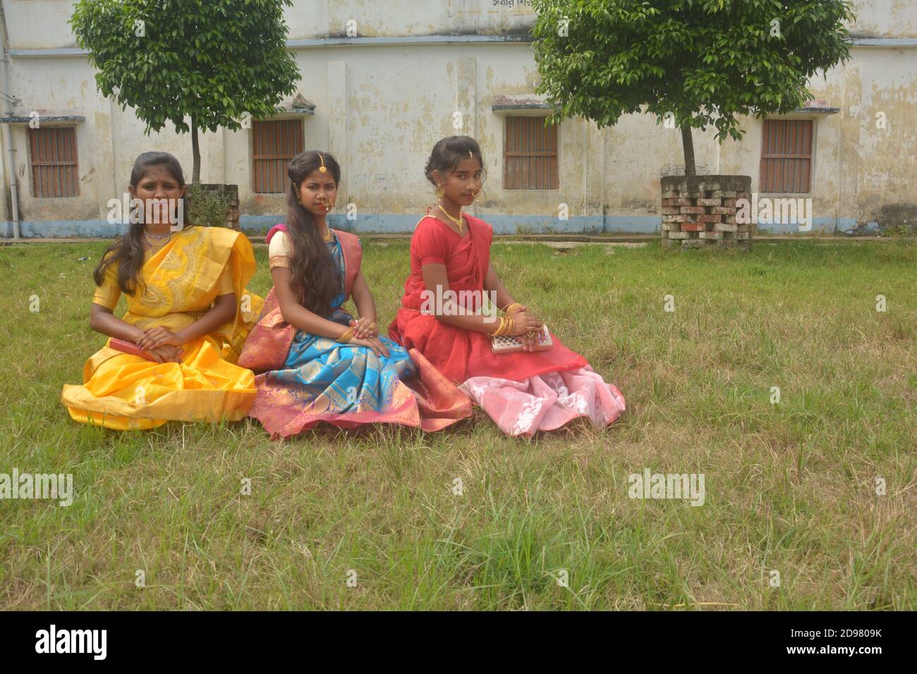 Nahaufnahme von drei Teenager-Mädchen in Indien tragen Sari und goldenen Nasenring Maang Tikka Halskette Ohrringe mit Make-up sitzen auf Feld, selektive Fokus. Stockfoto