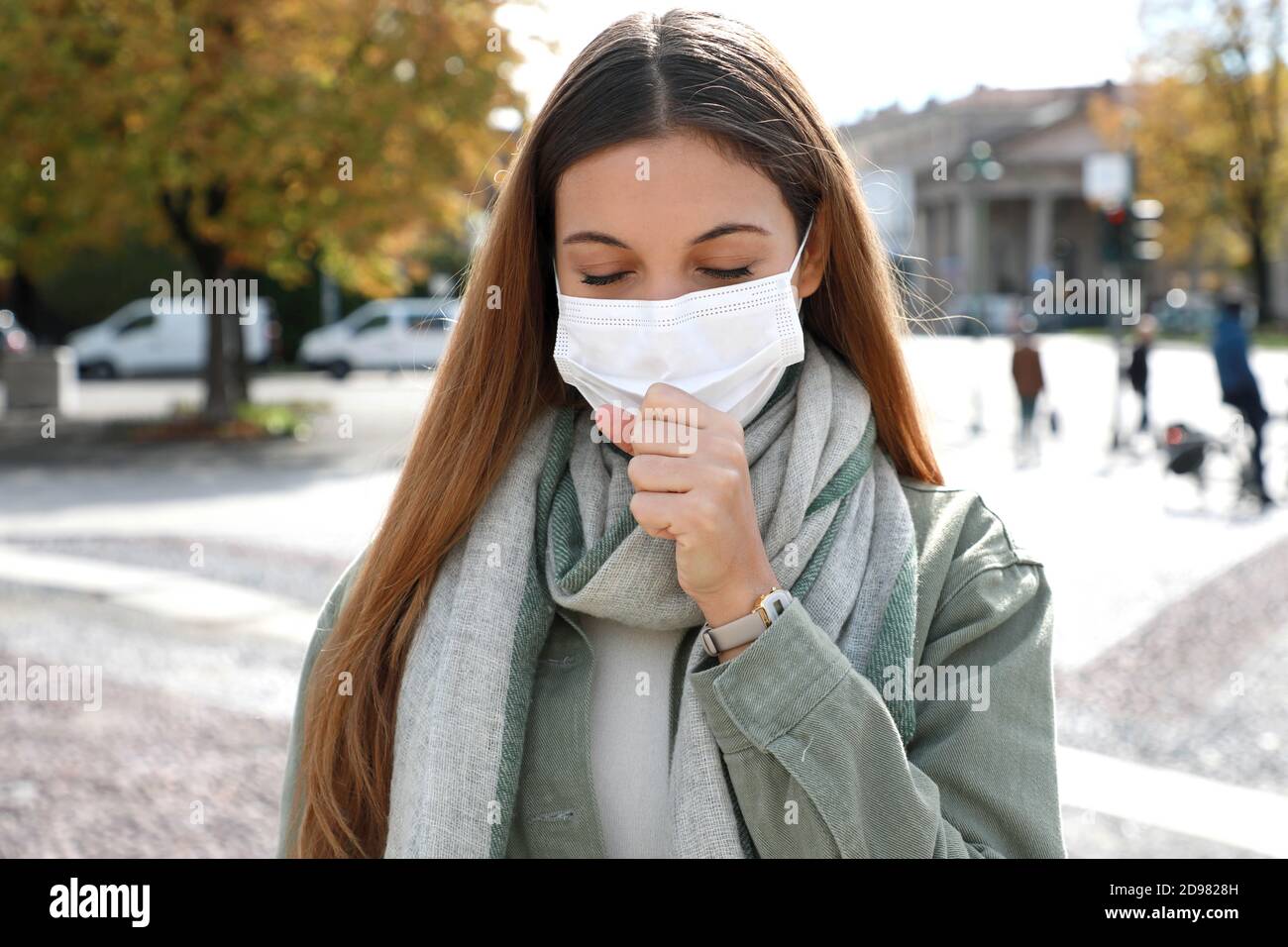 COVID-19 Junge Frau hustet mit chirurgischer Maske während der Coronavirus-Pandemie-Krankheit in der Stadt Straße. Mädchen mit Symptomen wie Husten und Kopfschmerzen. Stockfoto