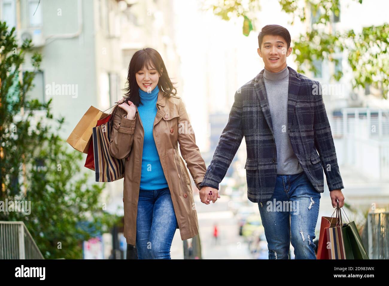 Glückliches junges asiatisches Paar, das auf der Straße in der Stadt läuft Mit Einkaufstaschen in den Händen Stockfoto