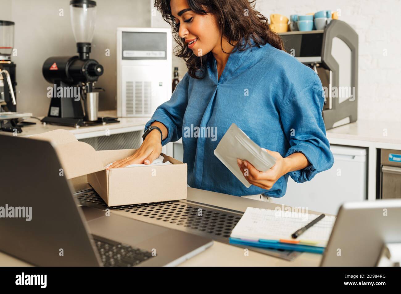 Der junge Unternehmer legt eine Packung Kaffee in einen Karton für den Versand. Coffee Shop Besitzer bereitet Online-Bestellung vor. Stockfoto