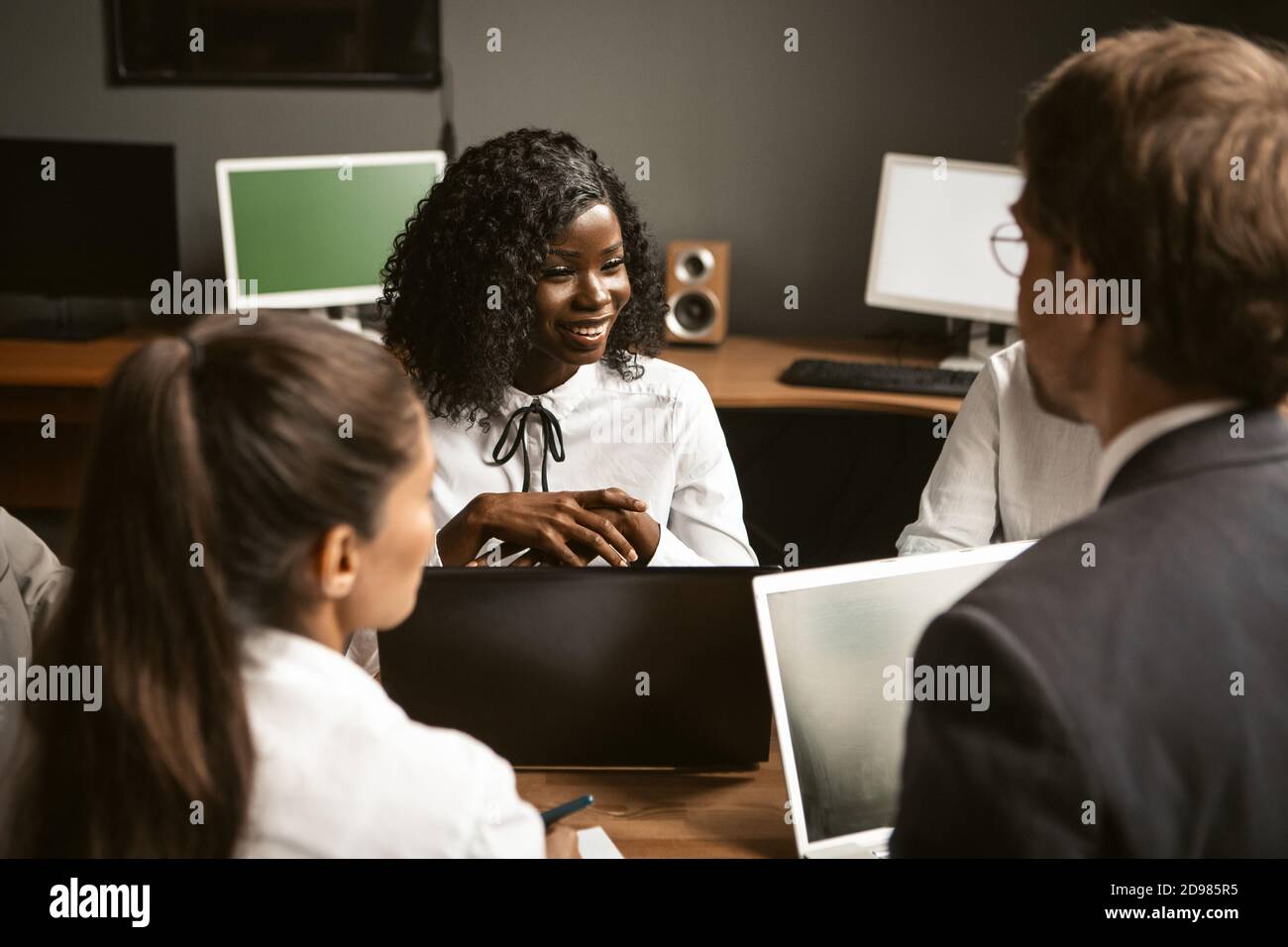 Lächelnde Geschäftsleute unterhalten sich am gleichen Schreibtisch im Büro. Brainstorming-Konzept. Teamwork-Konzept Stockfoto