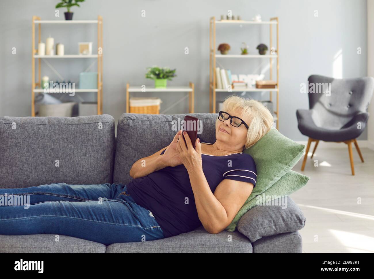 Glückliche reife Frau entspannen auf dem Sofa und Online-Shopping oder Videoanrufe bei Verwandten auf dem Handy Stockfoto