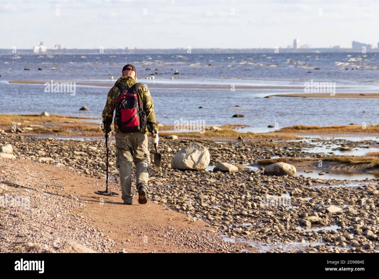 Ein Schatzsucher mit einem Metalldetektor geht am menschenleeren Sandstrand entlang auf der Suche nach verlorenen Münzen und Schmuck. Stockfoto