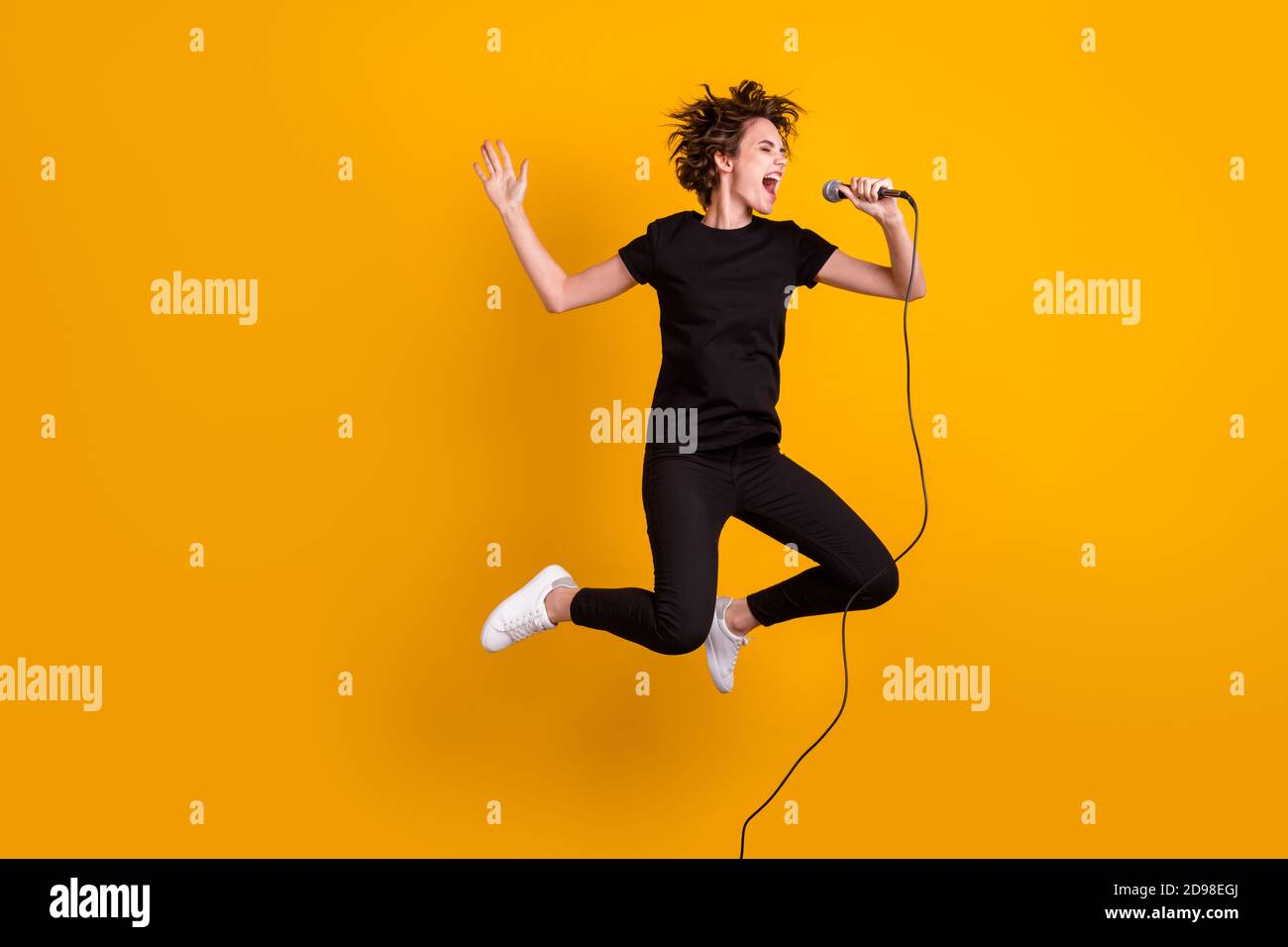 In voller Länge Körpergröße Ansicht der Skinny überglücklich fröhlich funky Mädchen springen Singing Single isoliert helle gelbe Farbe Hintergrund Stockfoto