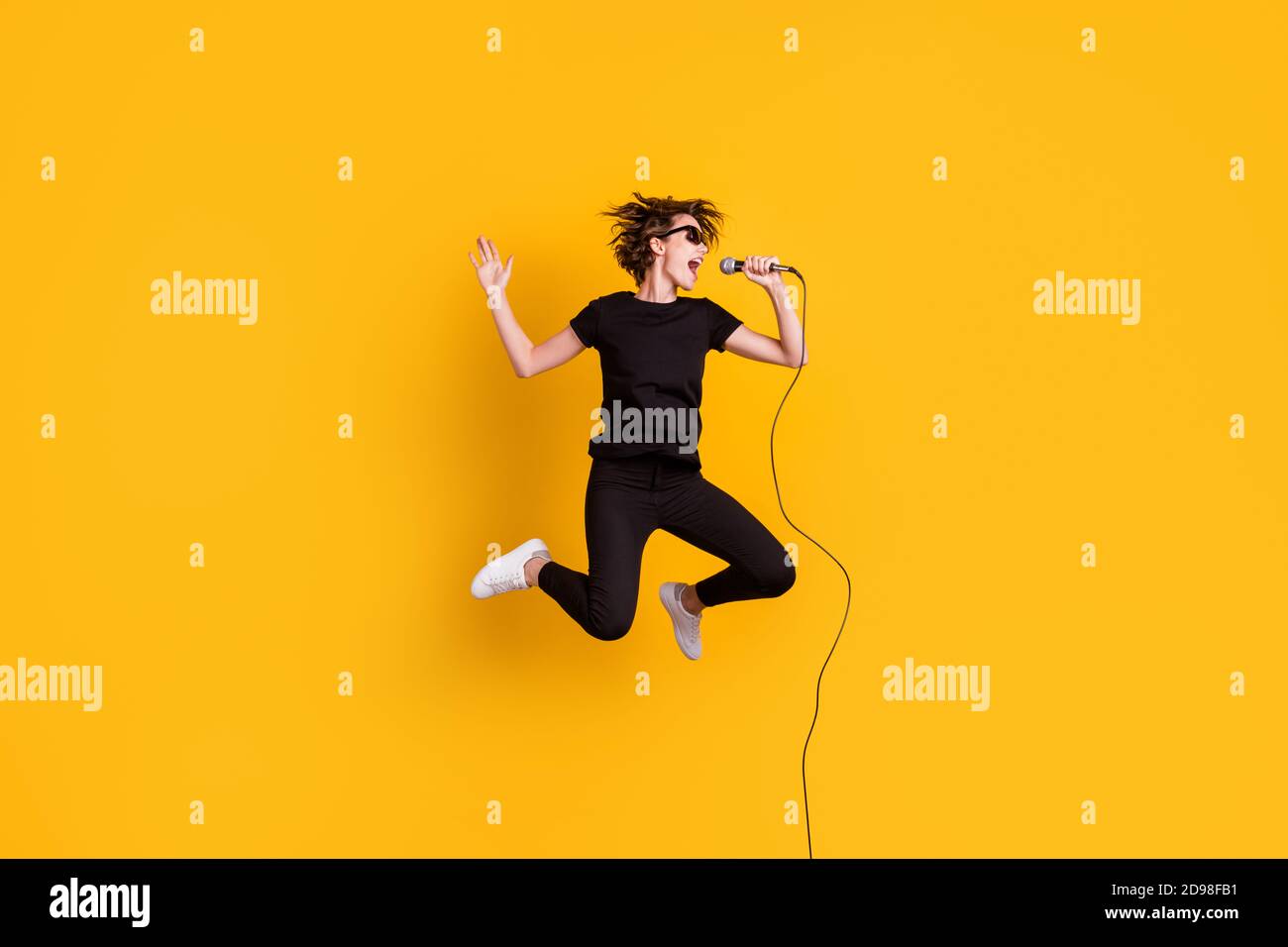 In voller Länge Körpergröße Ansicht der Skinny funky talentiert beliebt Mädchen springen singen live Hit isoliert über helle gelbe Farbe Hintergrund Stockfoto