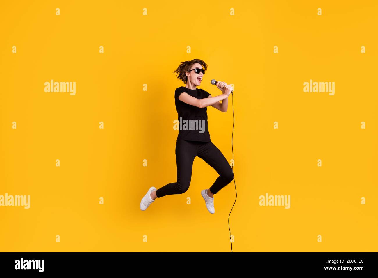 In voller Länge Körpergröße Ansicht der Skinny funky fröhliche Mädchen Springen singen Konzert Rock Sound isoliert hellen gelben Hintergrund Stockfoto