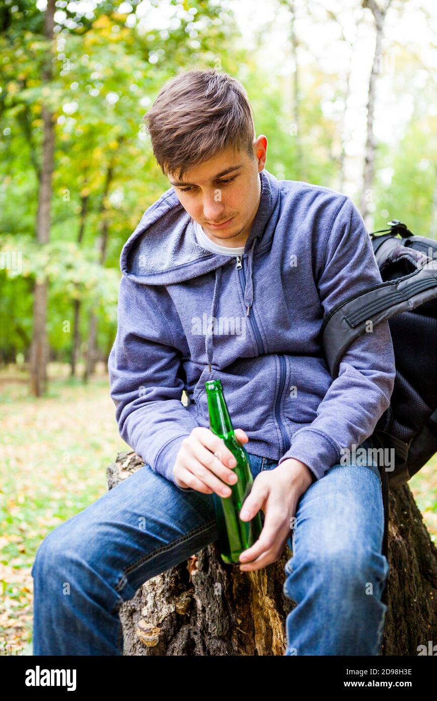 Trauriger junger Mann mit einer Flasche Bier Der Wald allein Stockfoto