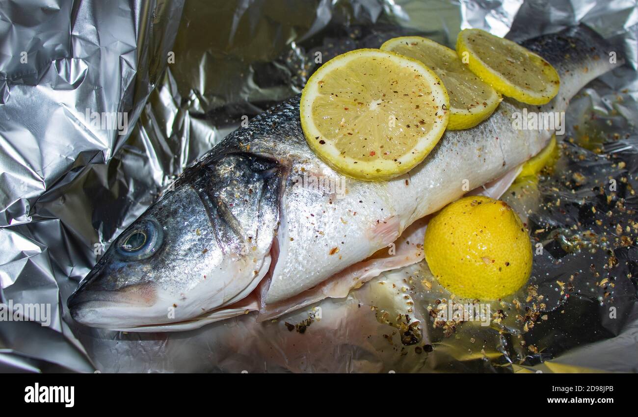 Frischer Seebarsch mit Zitrone und Gewürzen auf Aluminiumfolie. Kochen Stockfoto