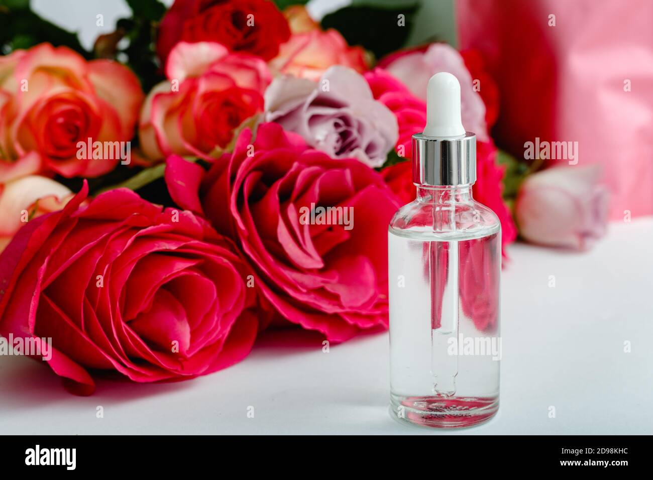 Serum auf weißem Tisch floralen Hintergrund. Blume rot rosa Rosen natürliche Schönheit Produkt. Hautpflege, Körperbehandlung. Glas Kosmetikflasche mit Rose Kopie Stockfoto