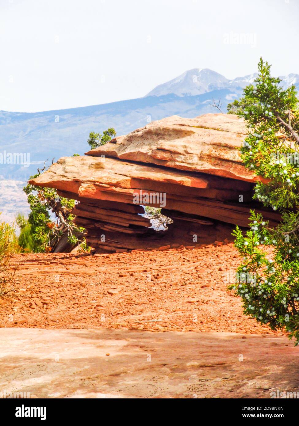 Eine verwitterte Felsformation, die einen kleinen Bogen bildet, bei Dead Horse Point, Utah, mit den schneebedeckten La Sal Bergen im Hintergrund Stockfoto