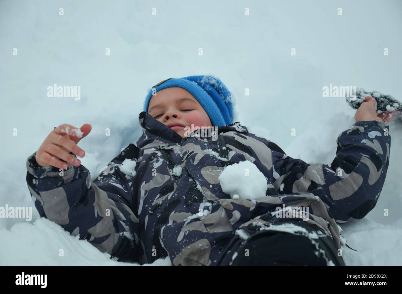 Happy Baby im Schnee liegen. Winter und Kälte. Stockfoto