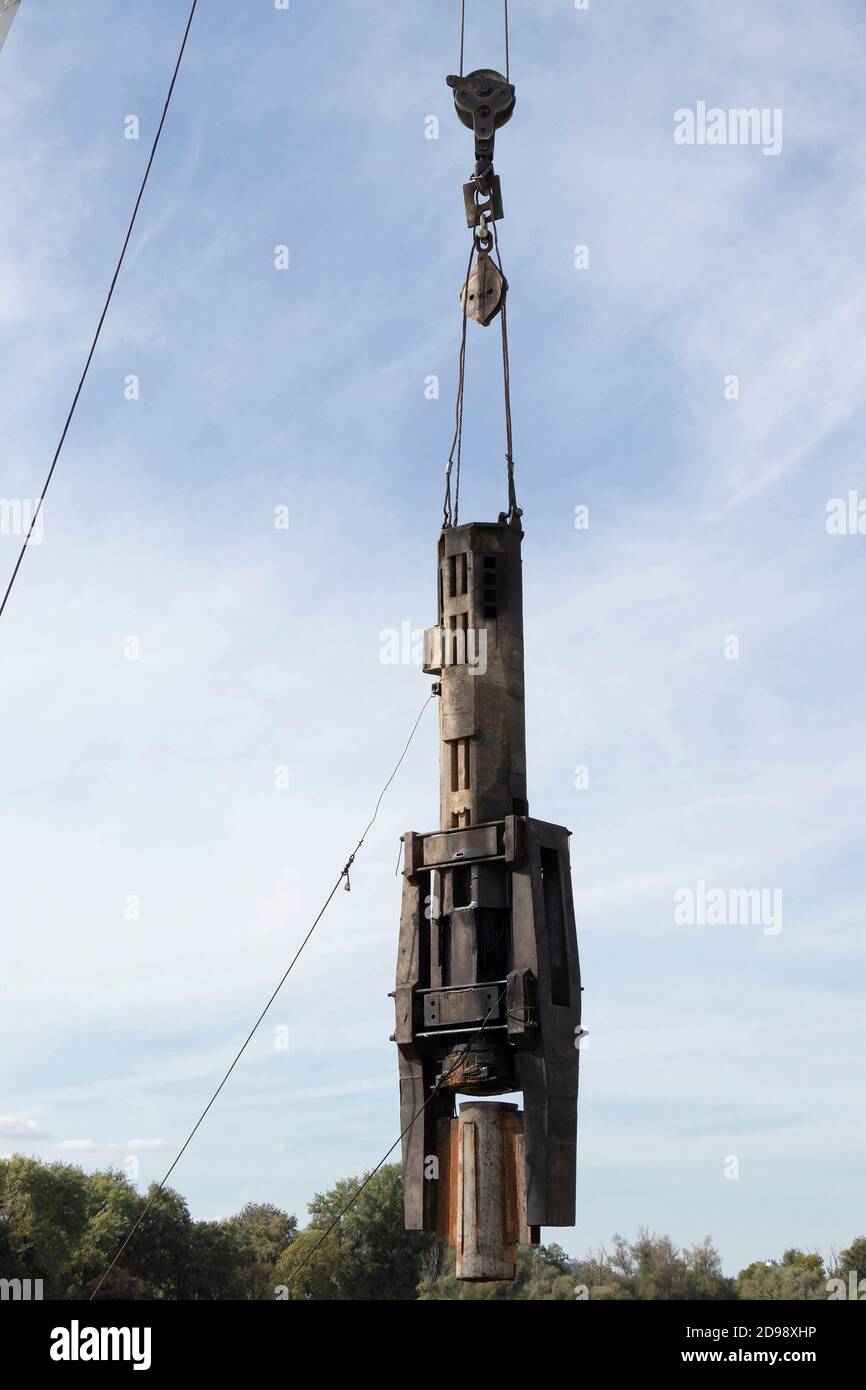 Baukran mit einem Haken und einem großen Stahlindustriespieß, der an Seilen hängt, die nach oben heben, niedrige Winkelansicht mit bewölktem Himmel Stockfoto