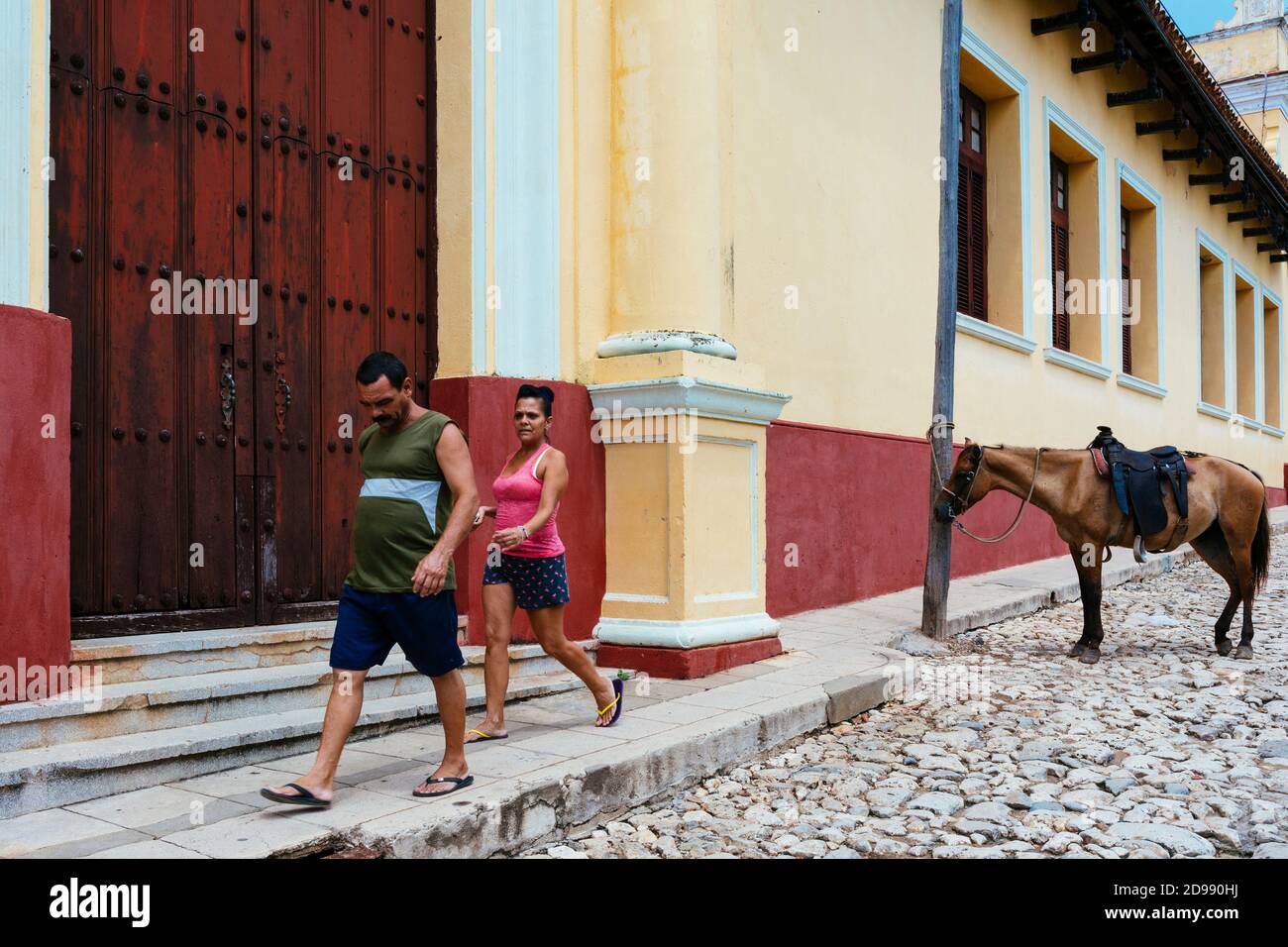 Der kubanische Mann und die kubanische Frau gehen die Straße entlang neben einem gefesselten Pferd. Trinidad, Sancti Spíritus, Kuba, Lateinamerika und die Karibik Stockfoto