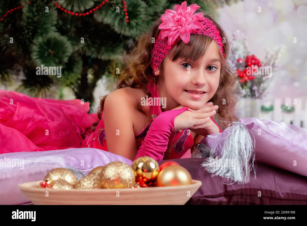 Schönes Mädchen im Ballkleid liegt in der Nähe des Weihnachtsbaums Auf Kissen Stockfoto