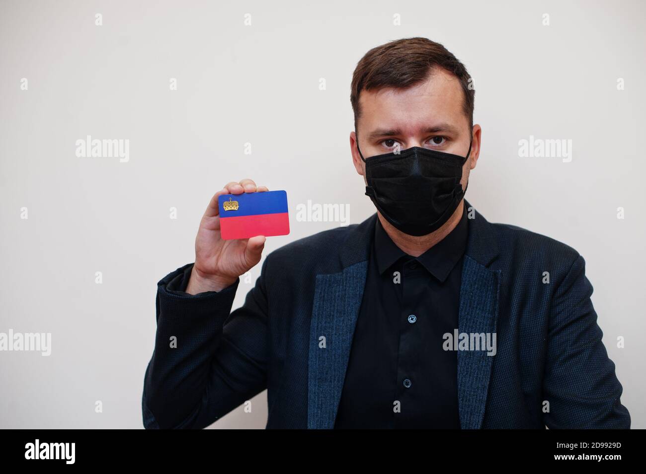 Europäische Mann tragen schwarz formell und schützen Gesichtsmaske, halten Liechtenstein Flagge Karte isoliert auf weißem Hintergrund. Europa Coronavirus Covid Land Konz Stockfoto