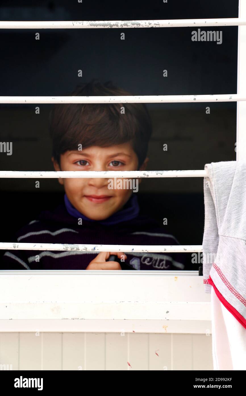 Ein Kind lächelt eifrig, ohne zu wissen, was die Zukunft bringt. Skaramagas beherbergt ein „vorübergehendes“ Flüchtlingslager, eine Art Warteraum, in dem Migranten, die hauptsächlich aus Syrien, dem Irak und Afghanistan kommen, sich aufhalten, bevor sie anderswo in Europa umgesiedelt werden. In Skaramagas können sie auch erfahren, ob ihr Antrag auf Umsiedlung genehmigt oder abgelehnt wurde. Makariou, Skaramagkas, Griechenland. Stockfoto