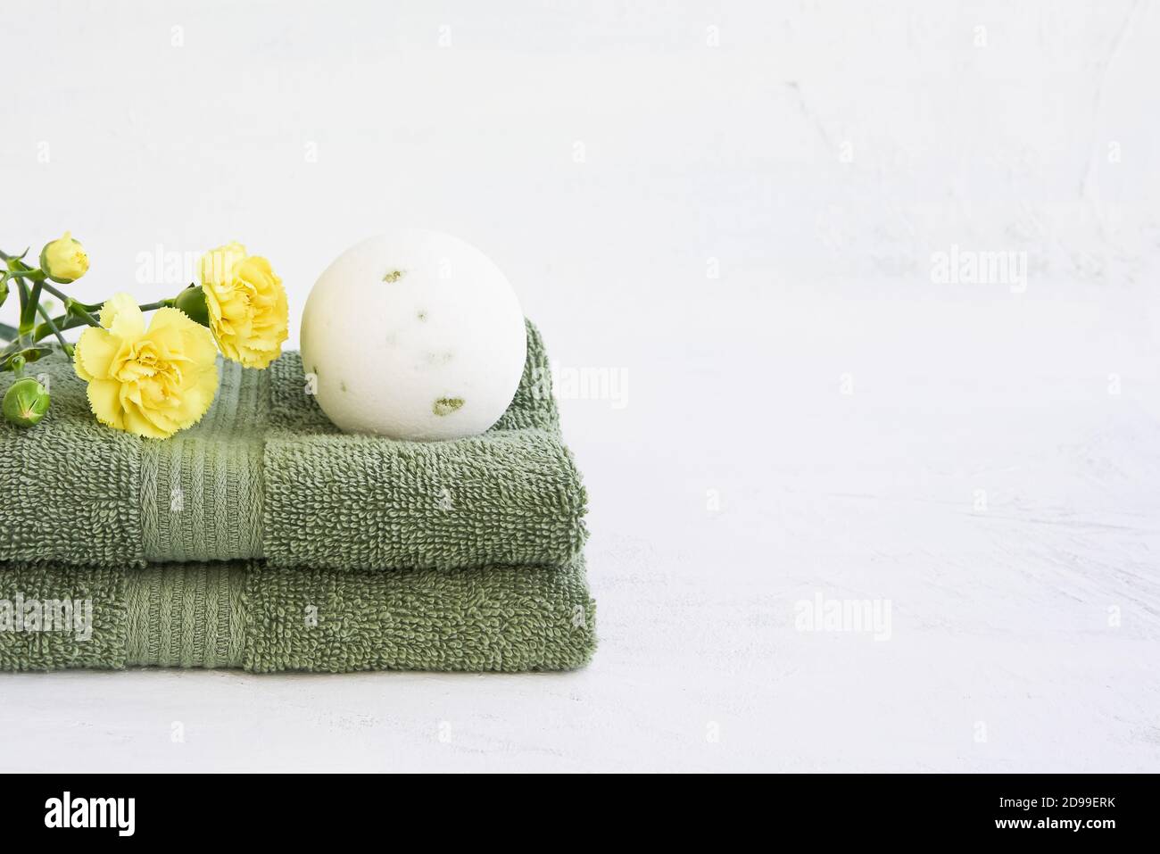 SPA-Konzept. Weiße Badebombe und zwei grüne Handtücher mit gelben Nelkenblumen auf weißem Hintergrund. Platz für Text kopieren Stockfoto