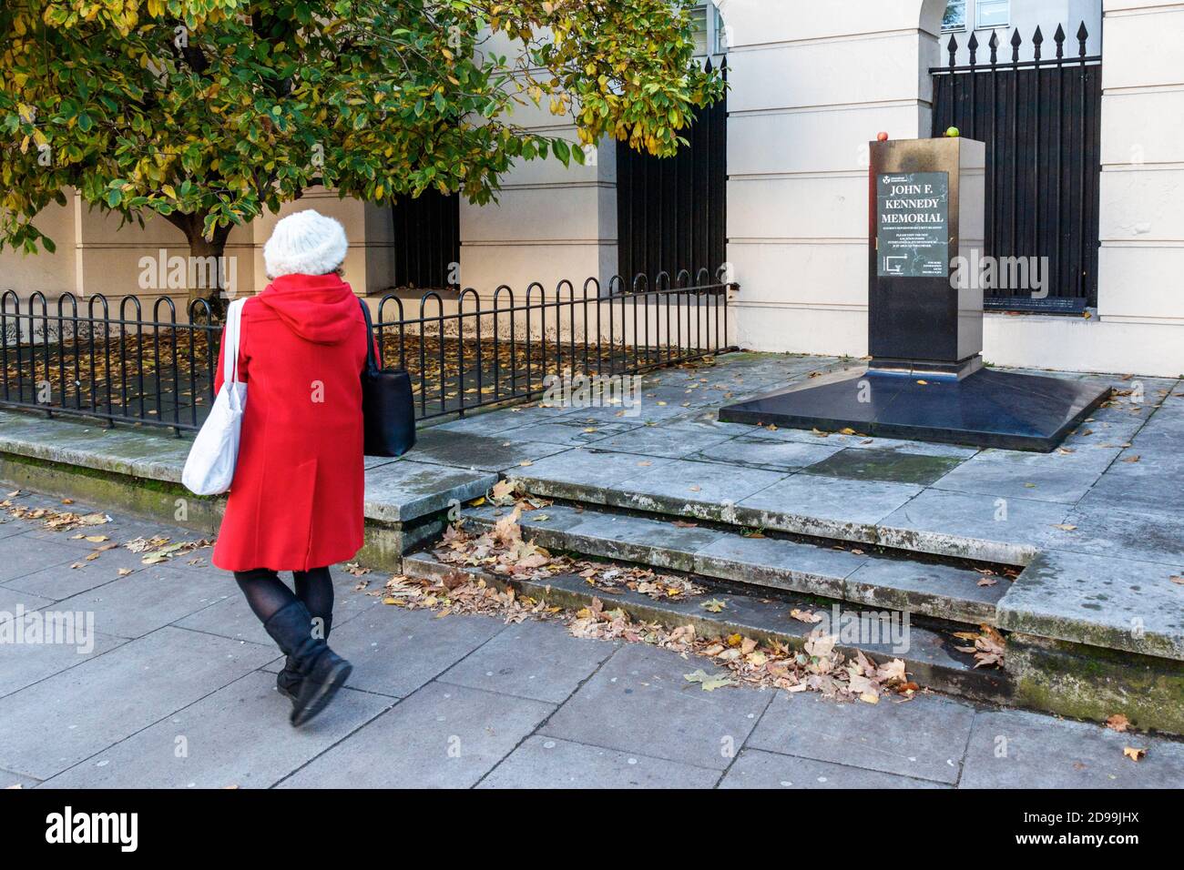 Eine Frau in einem roten Mantel geht am John F. Kennedy-Denkmal an der Marylebone Road vorbei, das aus Sicherheitsgründen aus seinem Sockel entfernt wurde, London, Großbritannien Stockfoto