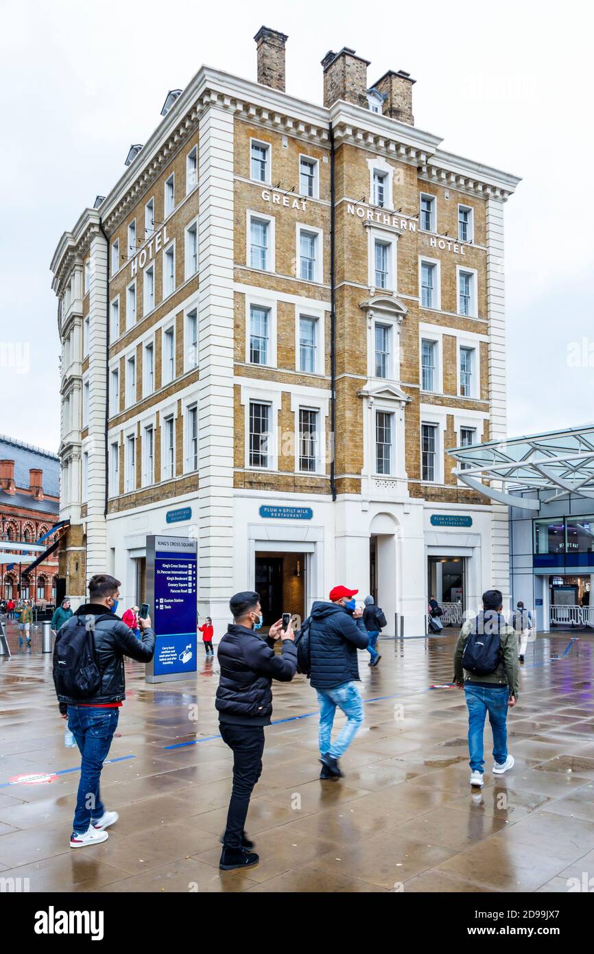 Touristen, die Gesichtsmasken tragen, machen Fotos auf ihren Handys vor dem Great Northern Hotel auf dem Vorplatz der King's Cross Station, London, Großbritannien Stockfoto