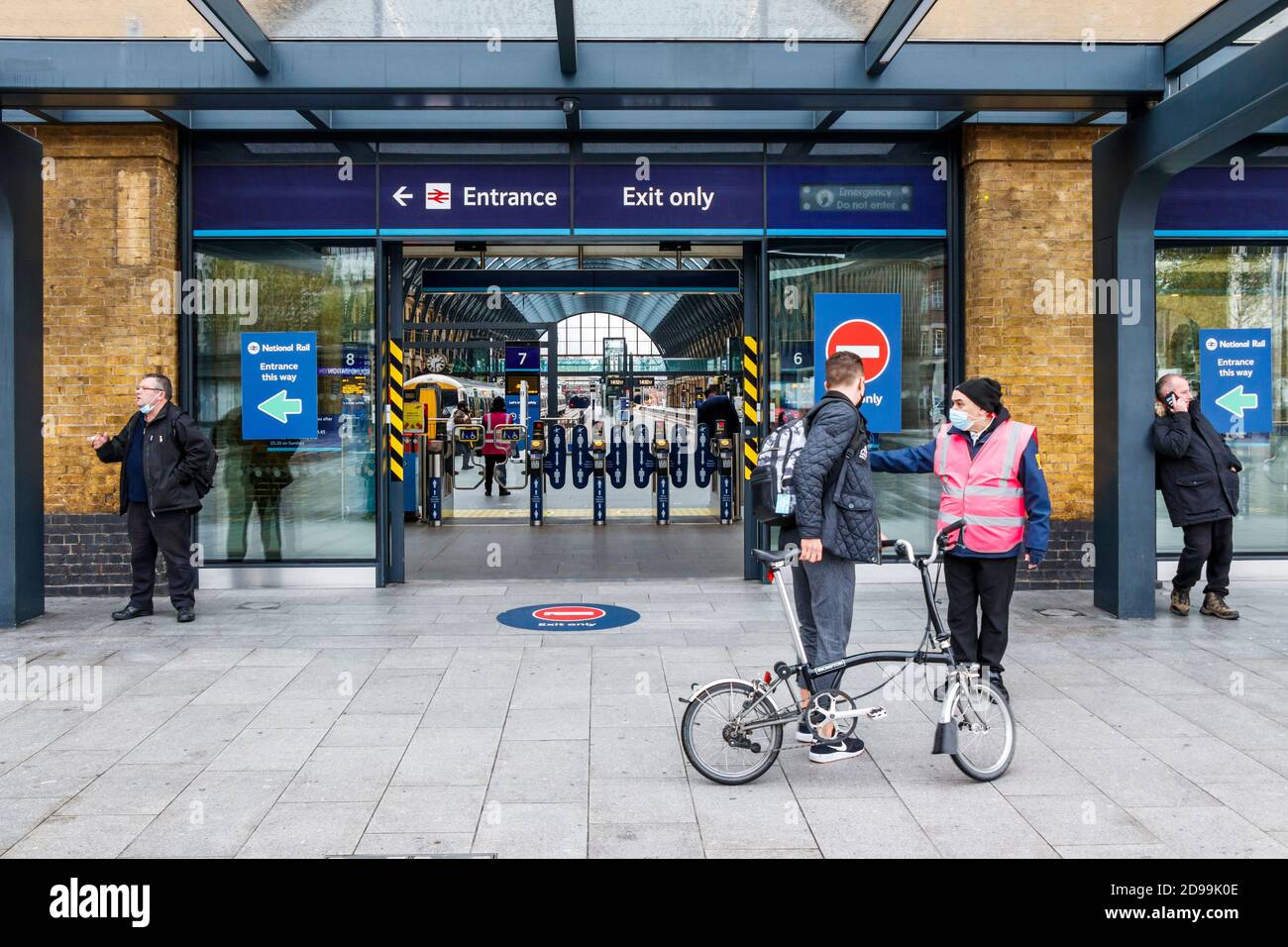 Ein Bahnangestellter hilft einem männlichen Radfahrer am Ausgang des Bahnhofs King's Cross, London, Großbritannien Stockfoto