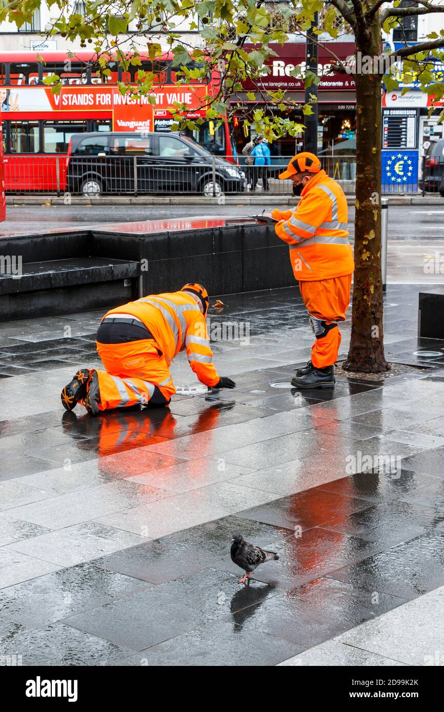 Zwei männliche Mitarbeiter von SGS in orangefarbener, gut sichtbarer Kleidung, die auf dem Vorplatz der King's Cross Station, London, Großbritannien, eine Inspektion durchführen Stockfoto