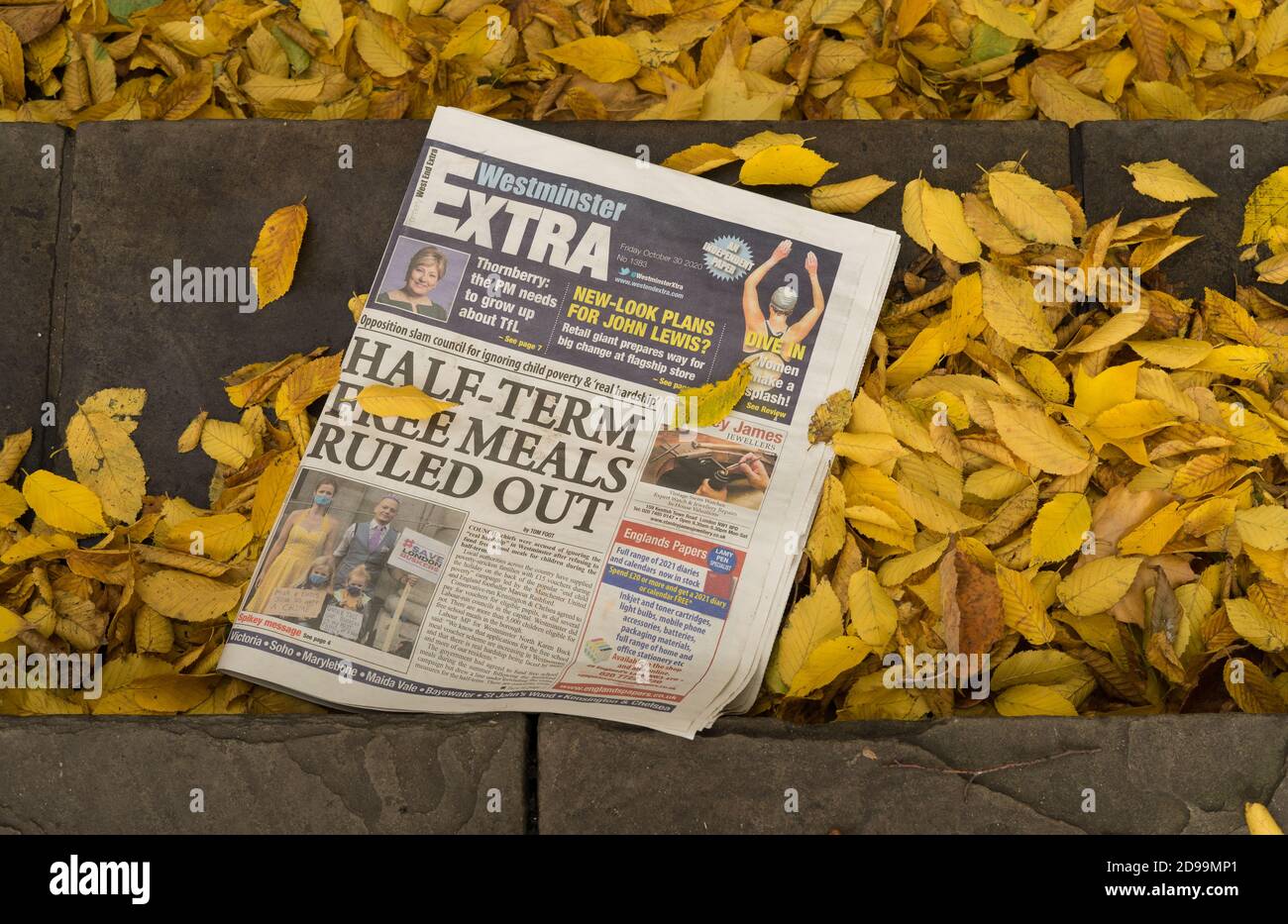 Alte weggeworfene Londoner Zeitung auf der Straße, umgeben von Herbstblättern. London Stockfoto