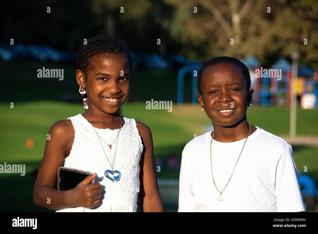 Ein Porträt von zwei afroamerikanischen Kindern, 8-10 Jahre alt, alle in weiß gekleidet. Wir sind gerade von einer Hochzeit im Park zurückgekommen. Brea, CA, USA Stockfoto