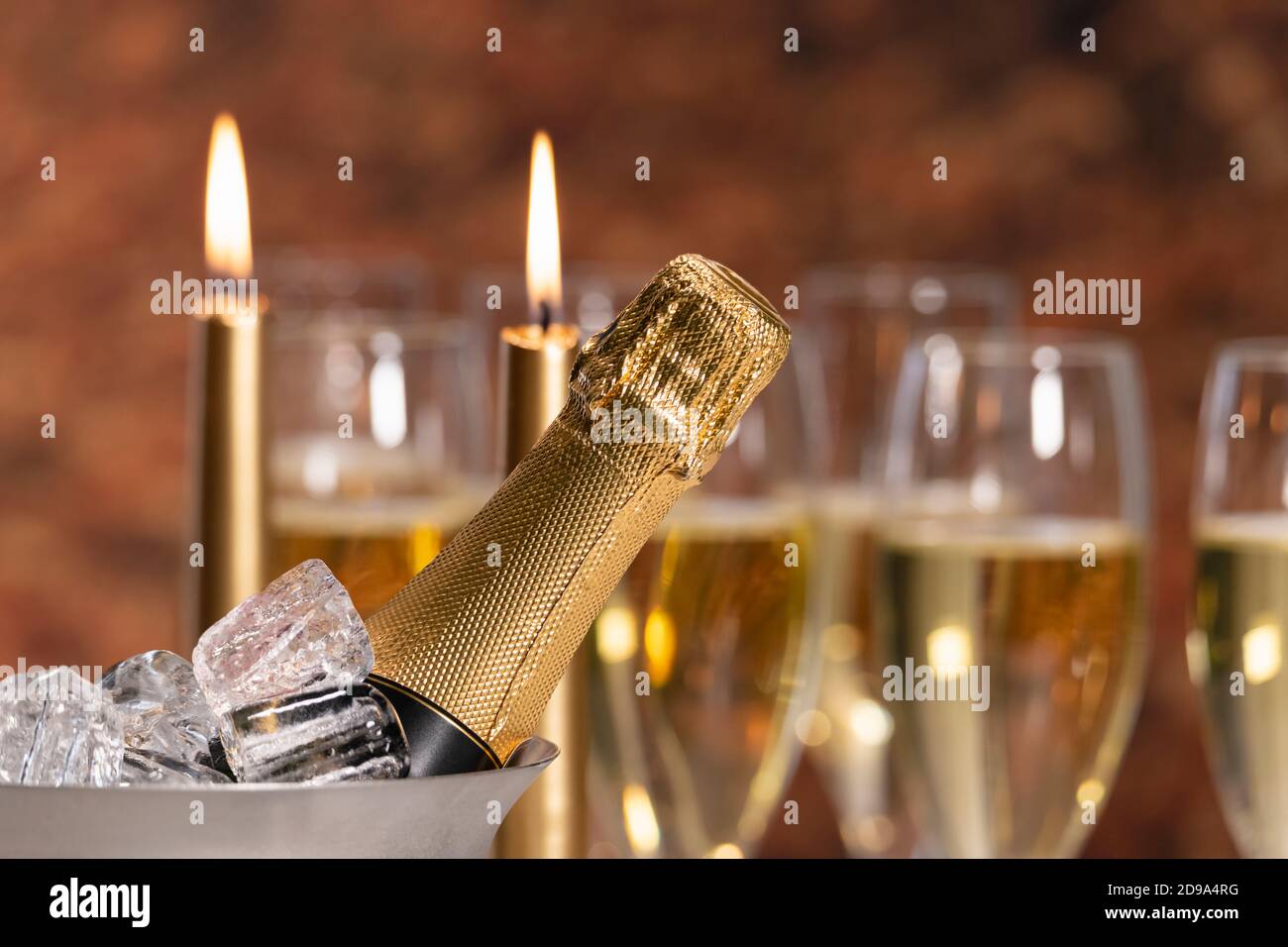 Selektiver Fokus eines Champagnerflaschenhalses in einem Champagnereimer mit Eis, mit außer Fokus angezündeten Kerzen auf der Rückseite. Alkohol und Feier Konzept. Stockfoto