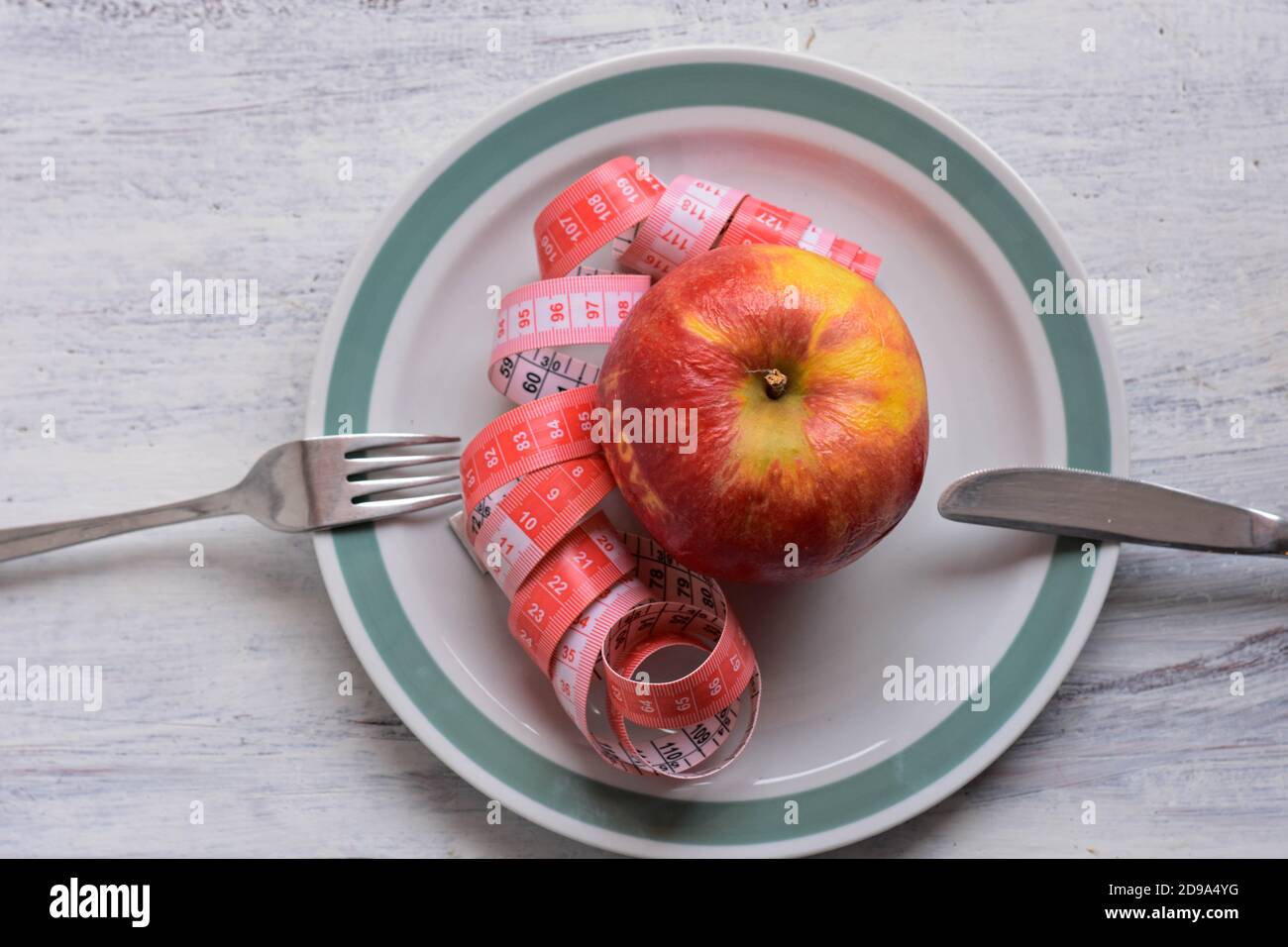 Apfel auf Schale mit Maßband, Messer und Gabel. Diätkost auf Holztisch. Gewichtskontrolle Stockfoto