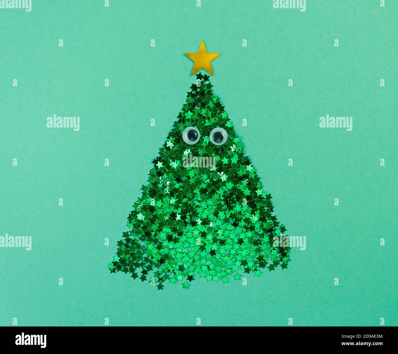 Weihnachtsbaumform aus Konfetti-Sternen mit Augen auf grünem Papier. Stockfoto