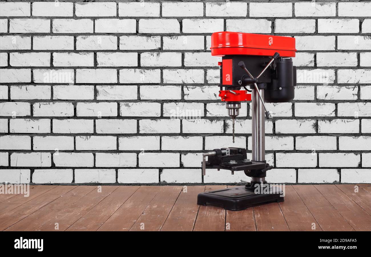 Das Werkzeug der Metallbearbeitung - die rote neue Bohrmaschine auf dem hölzernen Tisch und dem Hintergrund der weißen Ziegelwand. Stockfoto
