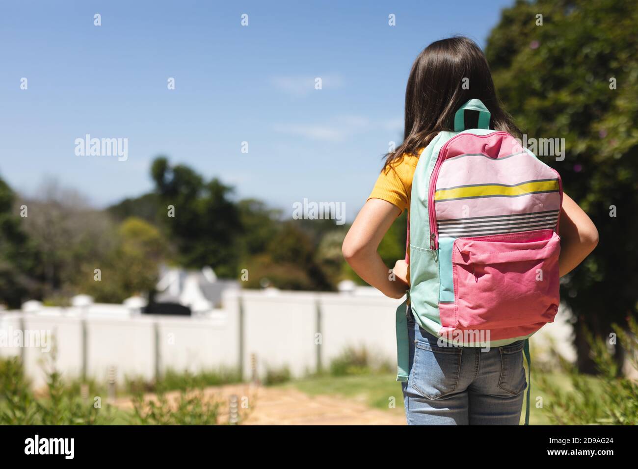 Kaukasisches Mädchen mit schulterlangen dunklen Haaren zu Fuß zur Schule Schultasche tragen Stockfoto