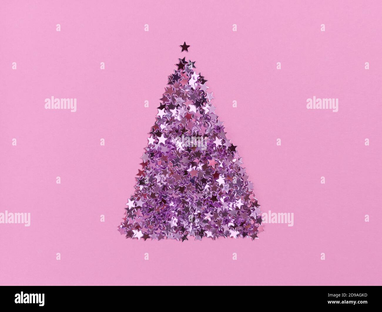 Weihnachtsbaumform aus Konfetti-Sternen auf rosa Papier. Festliche einfarbige flache Lay. Stockfoto